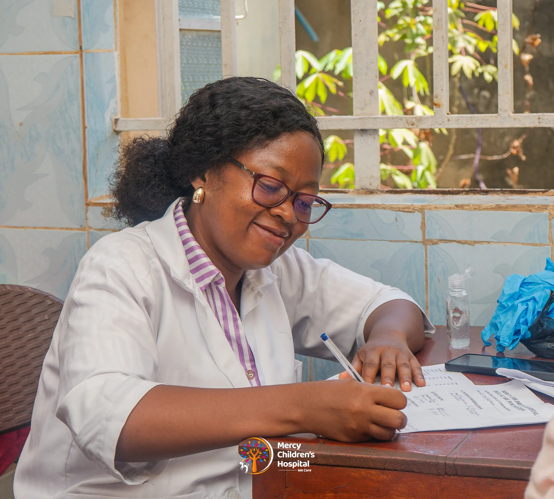 A paediatrician smiling while writing up notes at her desk