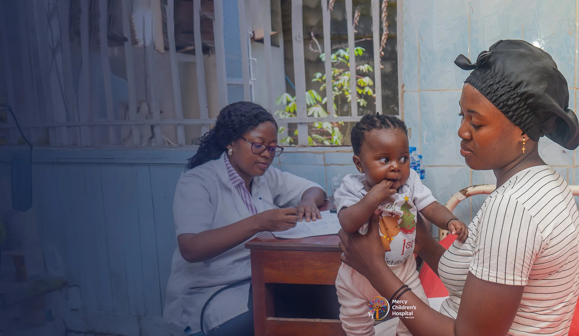 A paediatrician taking notes during a consultation while a mother holds her toddler